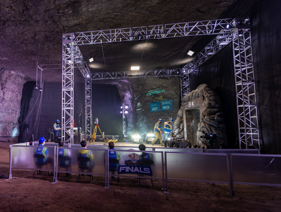 A large cave with a stage and a stone portal on one side, dramatically lit