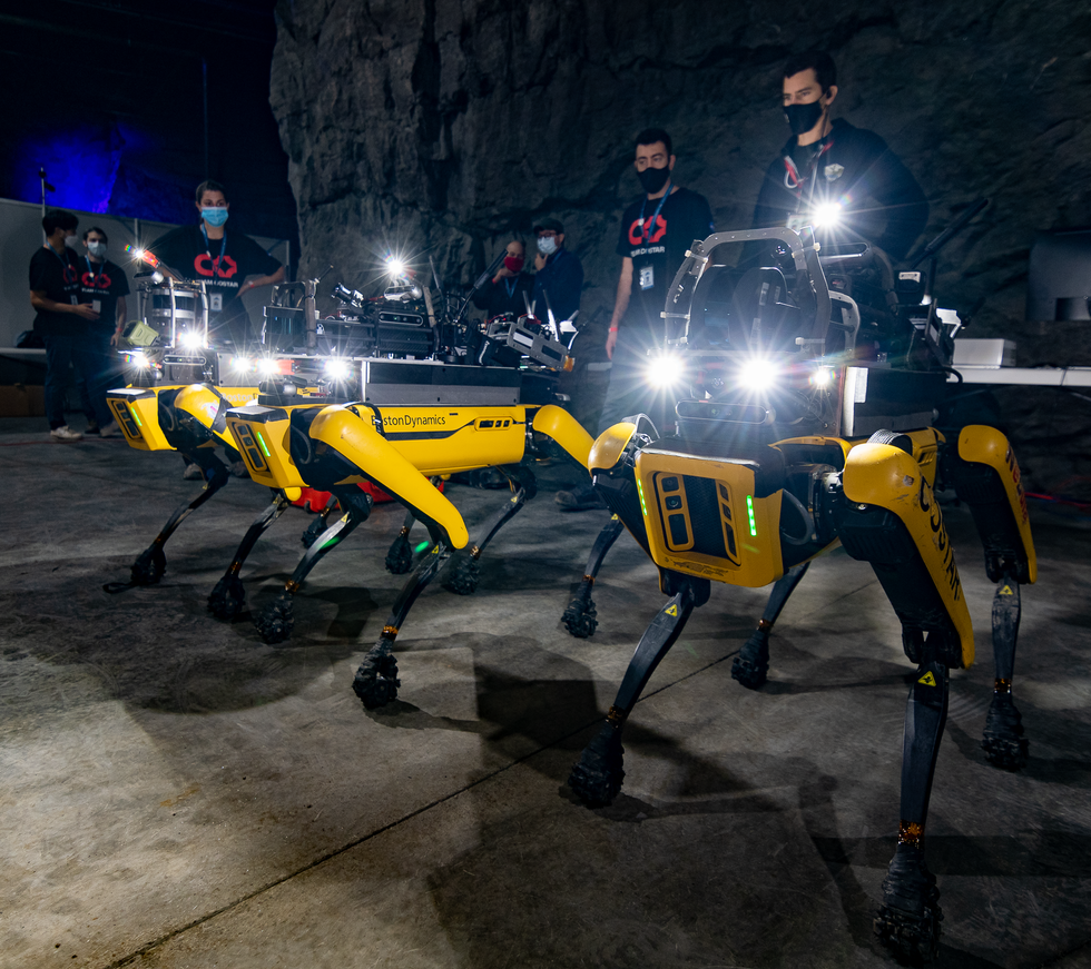 Four yellow quadrupedal robots standing with a group of humans