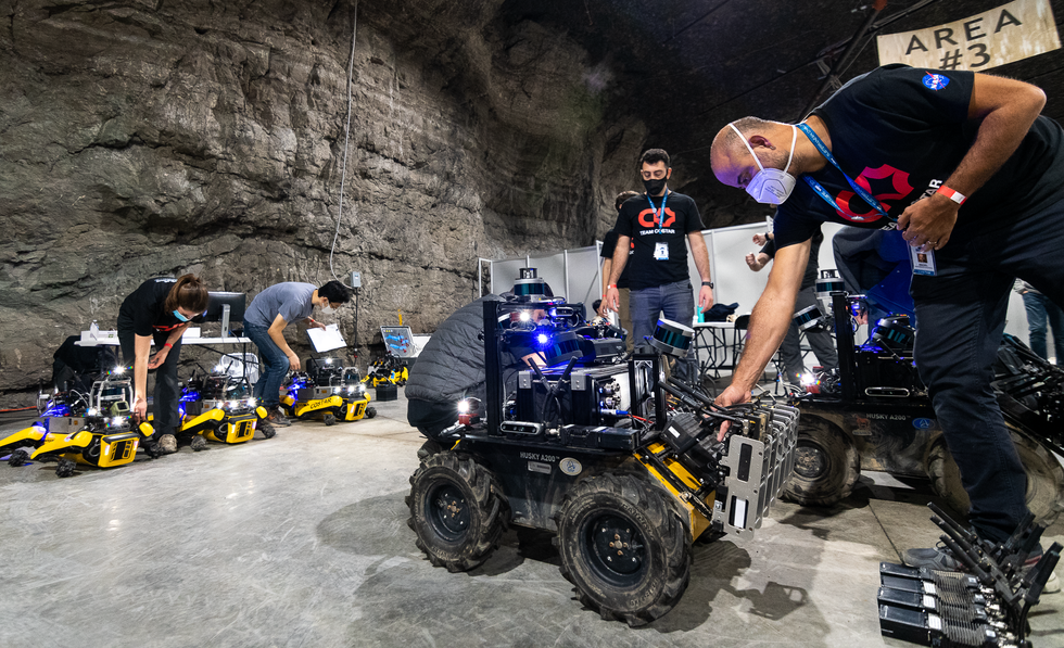Roboticists in a cave adjusting electronics on wheeled and legged robots