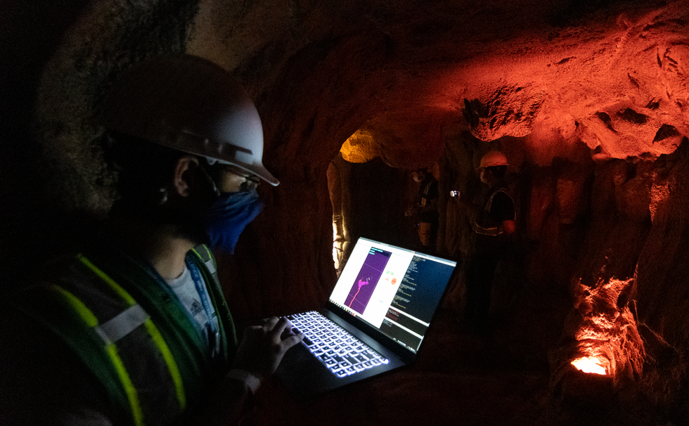 A roboticist looks at data on a laptop in a cave lit with a red light