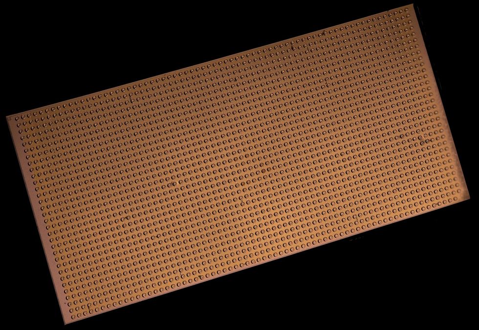 A magnified view of a gold rectangular chip with evenly spaced dots densely covering its surface