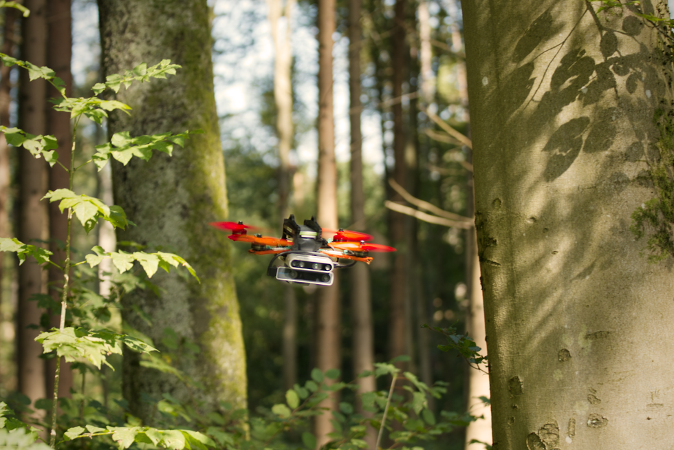 A colorful quadrotor drone flies through a forest