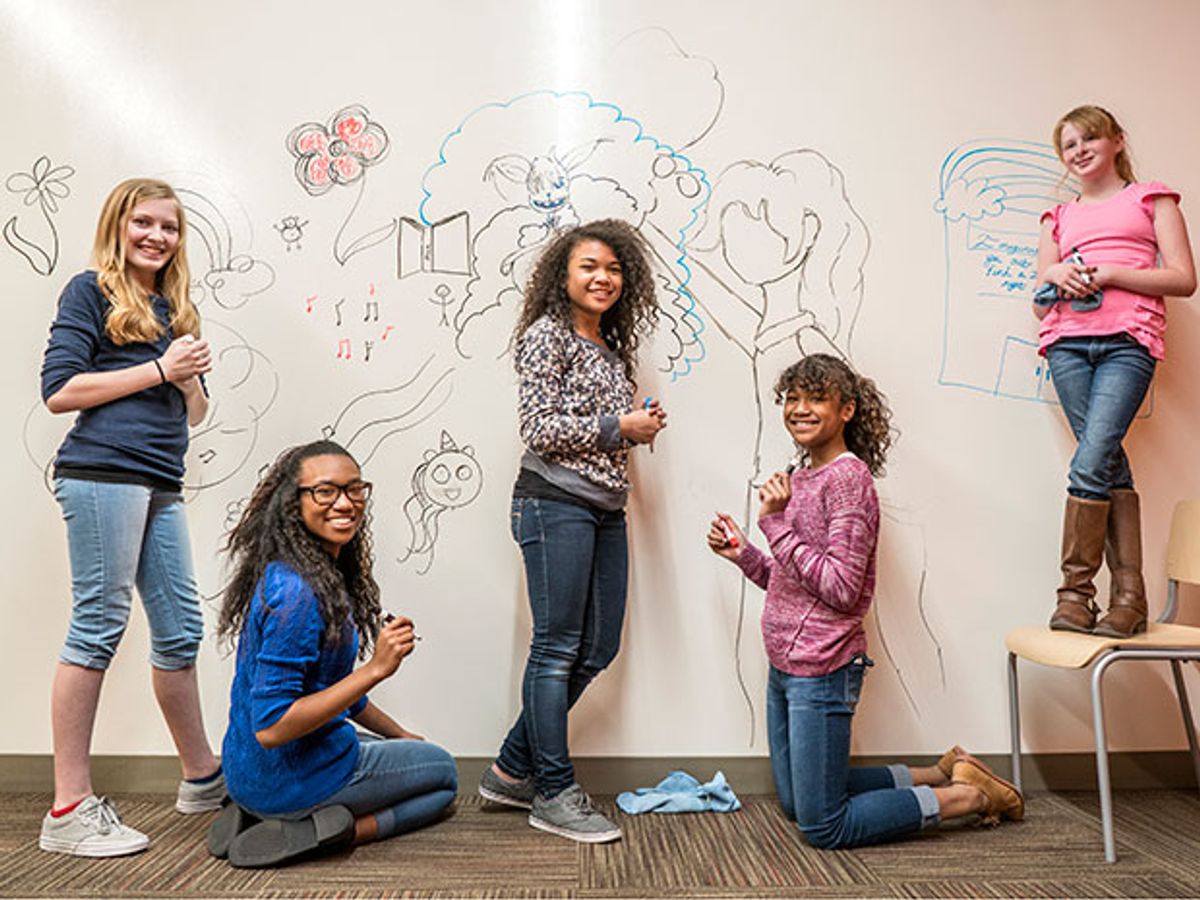 Five teen girls express themselves on a whiteboard wall, mixing art with engineering could attract girls like this to STEM careers