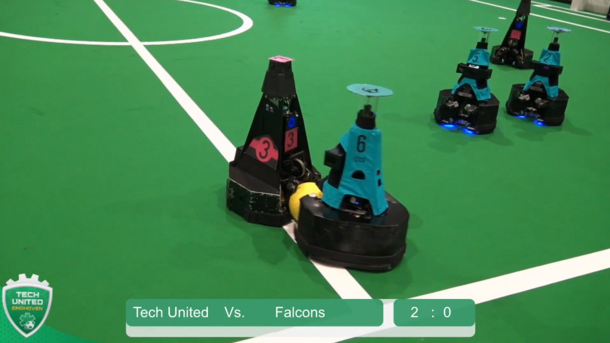 Five waist-high pyramidal mobile robots squabble over a yellow soccer ball on a green soccer field.