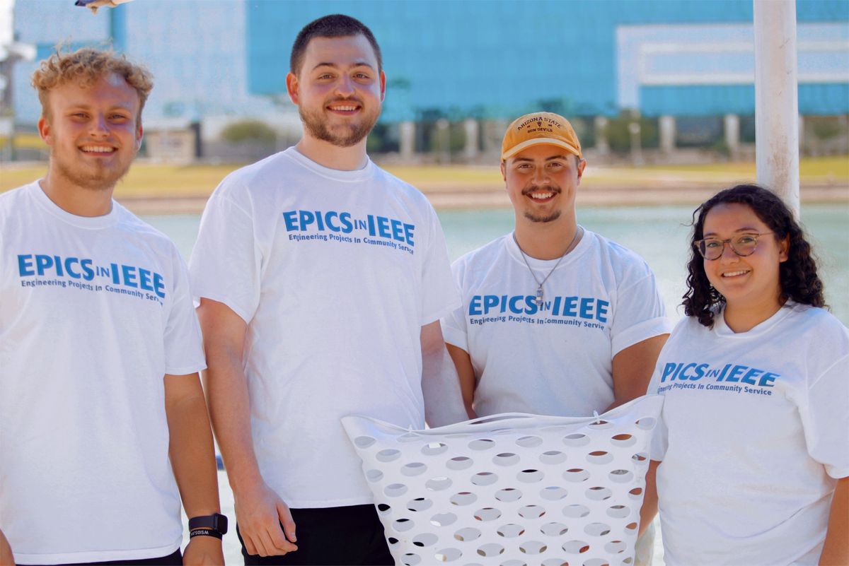 Four young people wearing white t-shirts that say EPICS in IEEE holding a robot