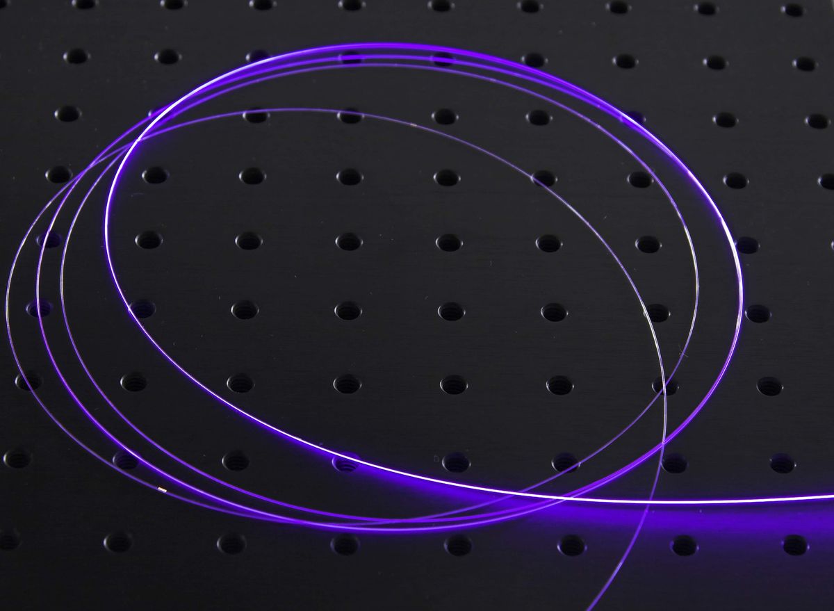 Glowing purple optical fiber curled on a black worktable with a grid of holes in it.