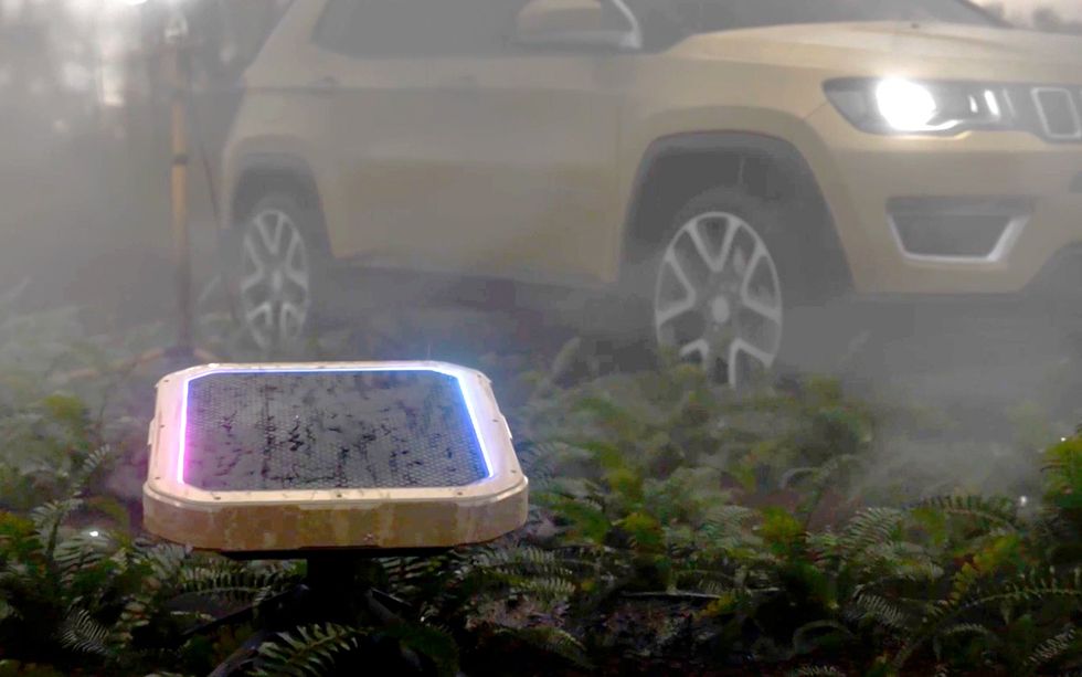 Greenerwave's RIS satellite internet ground terminal is a glowing rectangle with various round and square shapes on its surface, some plants in the foreground, and a car visible in the background.