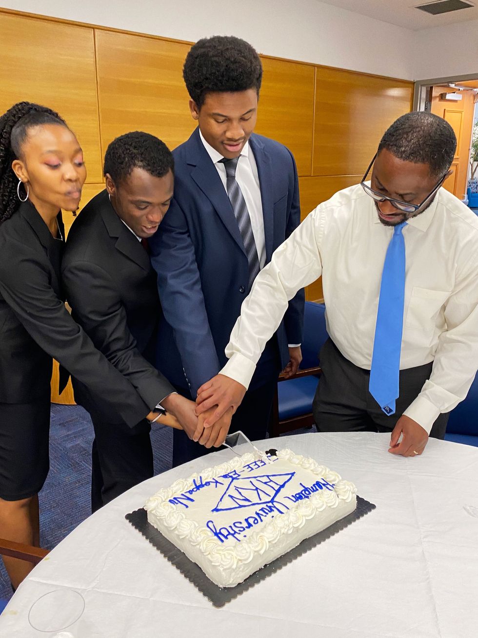 People holding knives and cutting white translucent cake with blue letters on it
