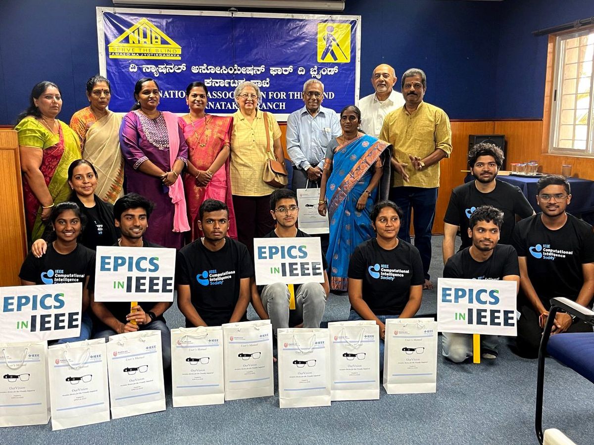 group of people standing in front of a banner, people sitting on floor in front holding signs that read “EPICS in IEEE”