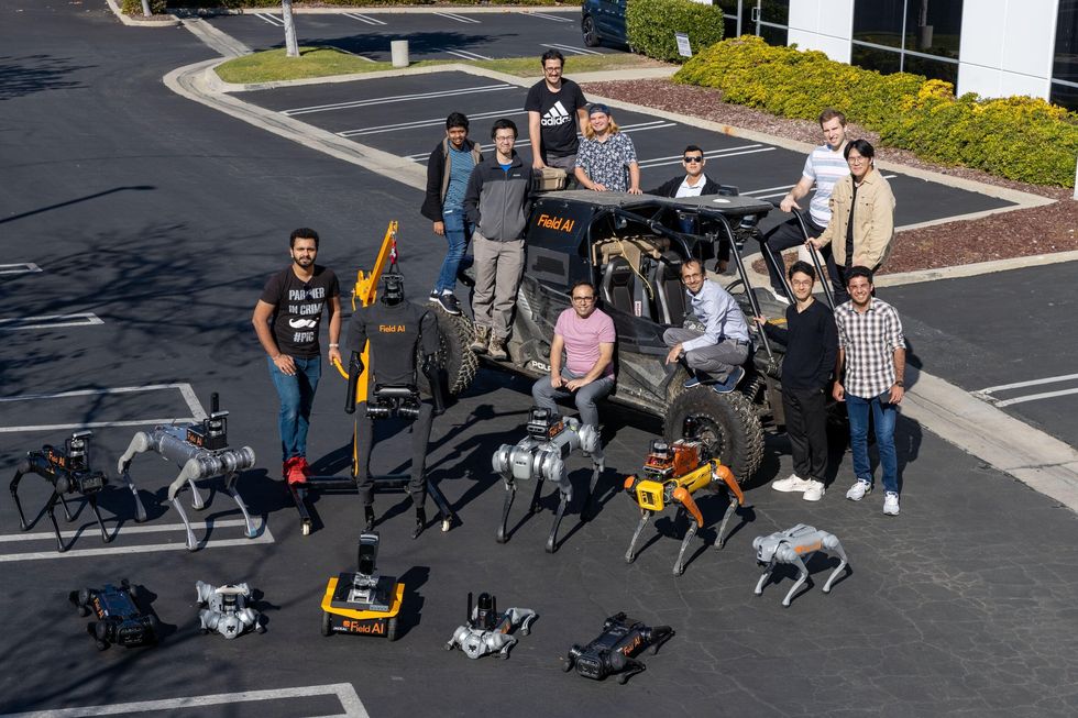 会社の駐車場で撮影された男性10名とロボット12体の集合写真