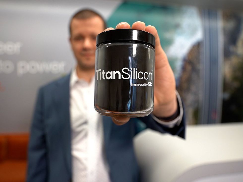hand holding a glass jar filled with a black substance that reads "Titan Silicon"