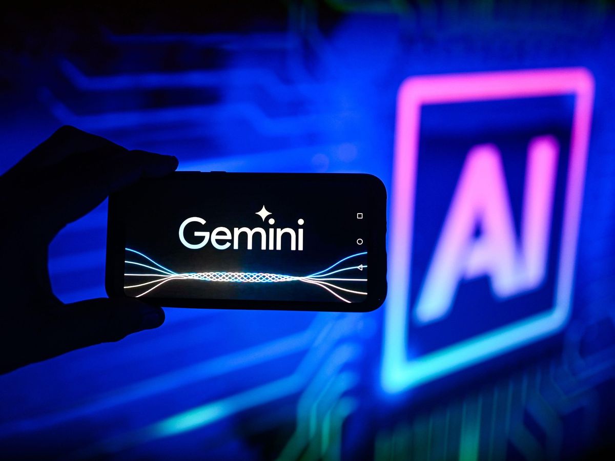 hand holding a phone that reads "Gemini" on the front with out of focus letters "AI" in the background