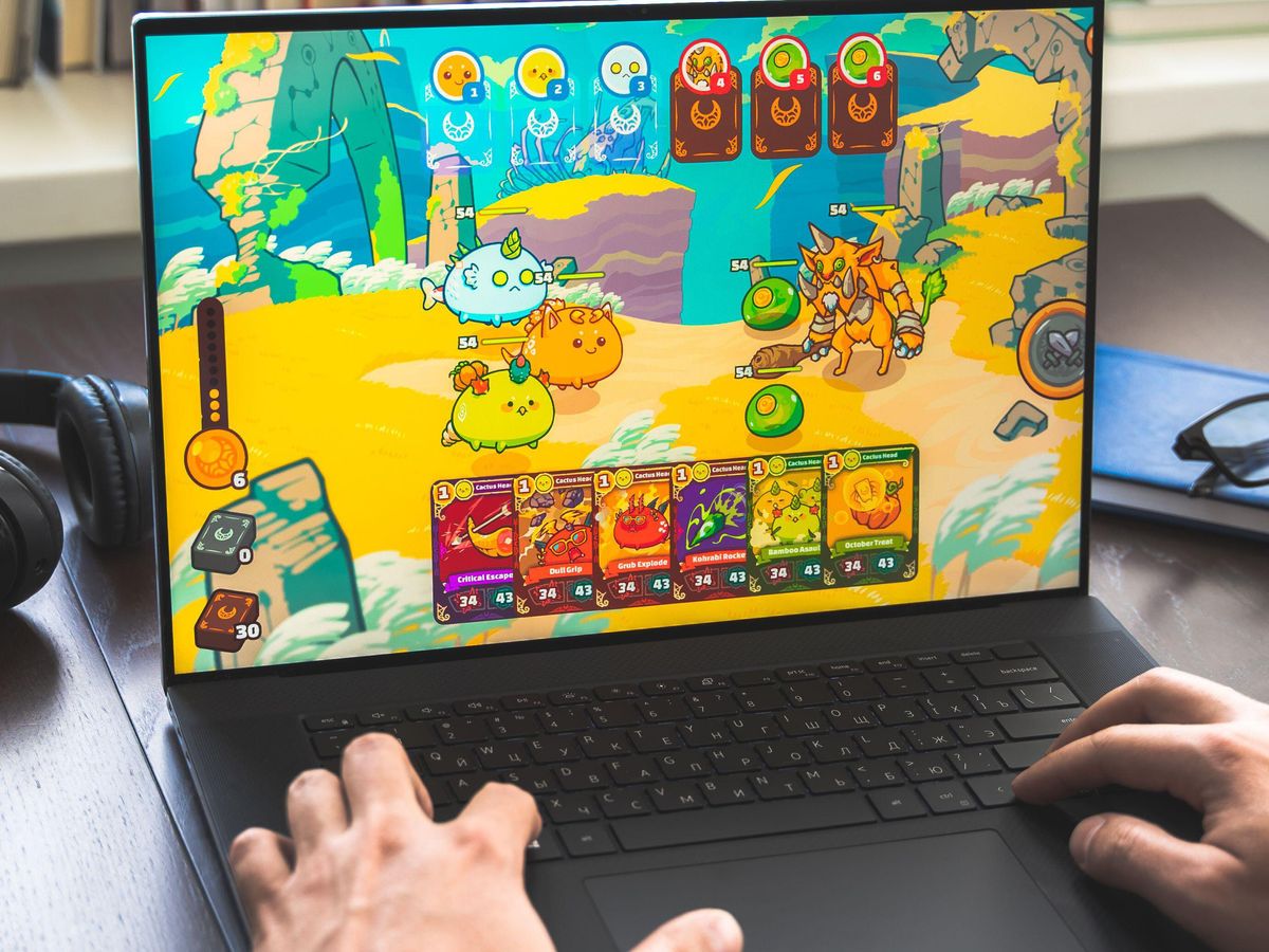 Hands on the keyboard of a laptop. A colorful video game with little creatures is on the screen.