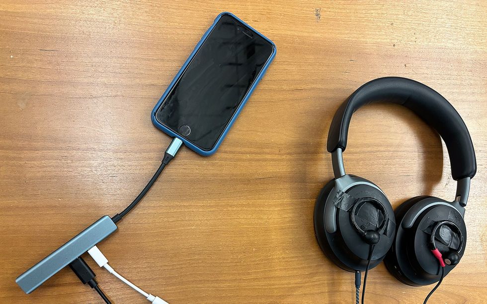 Headphones with one earbud taped to the exterior face of each speaker resting on a table next to a smart phone.
