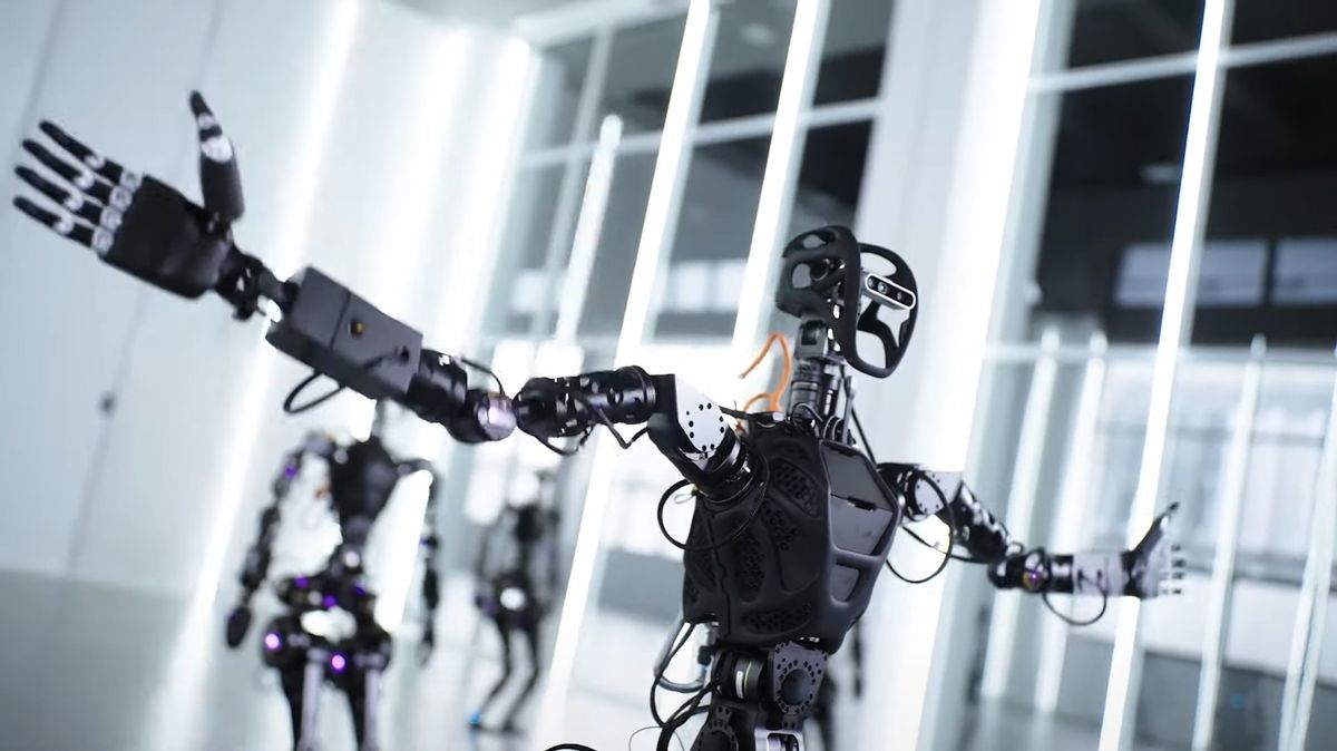 Humanoid robot pictured in foreground with arms wide open, two other humanoids behind it