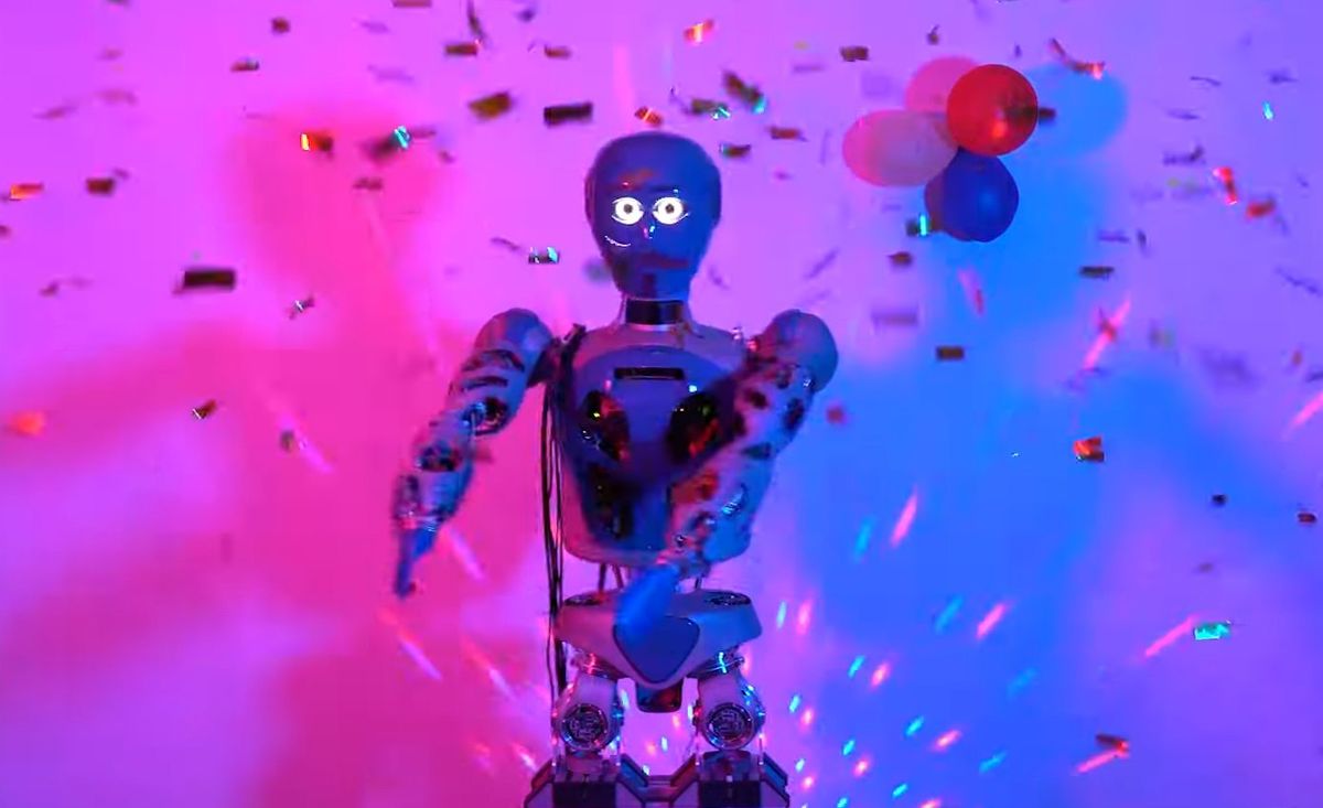 humanoid robot with googly white eyes extends arms toward camera in a dance club-like blue and pink lit scene with confetti and balloons in the background