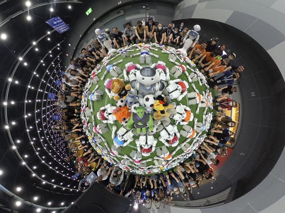 Humanoid robots and their human handlers gather in a circle for a group photo.