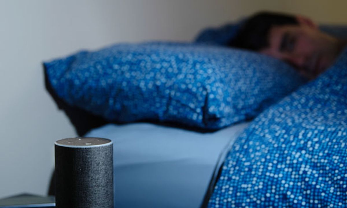 Image of Alexa sitting on a table next to a bed as someone sleeps.