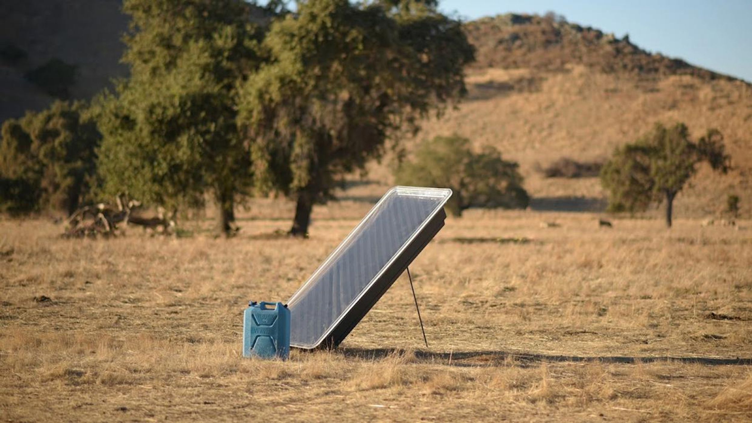 image of dry, summery landscape with water jug and solar water collector device propped up to point at the sun