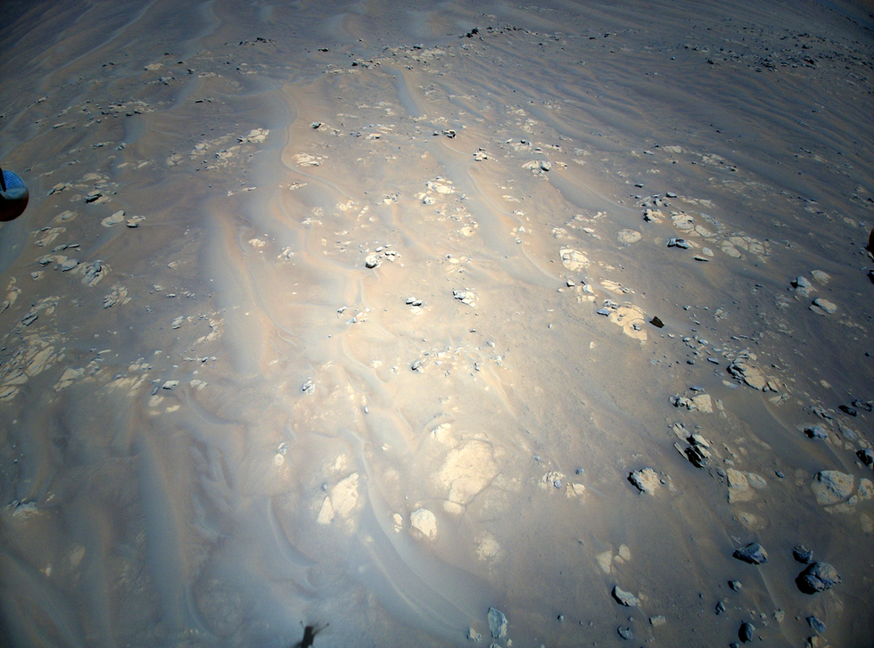 Image of the sandy, rocky surface of Mars, with the shadow of the Mars helicopter in flight at the bottom