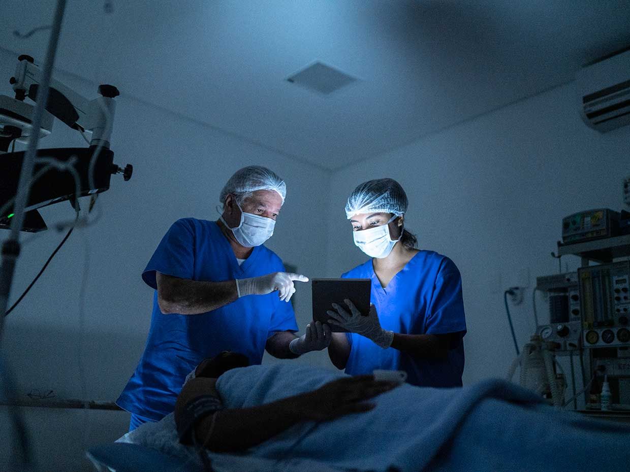 Photo of doctors looking at a tablet over a patient. 