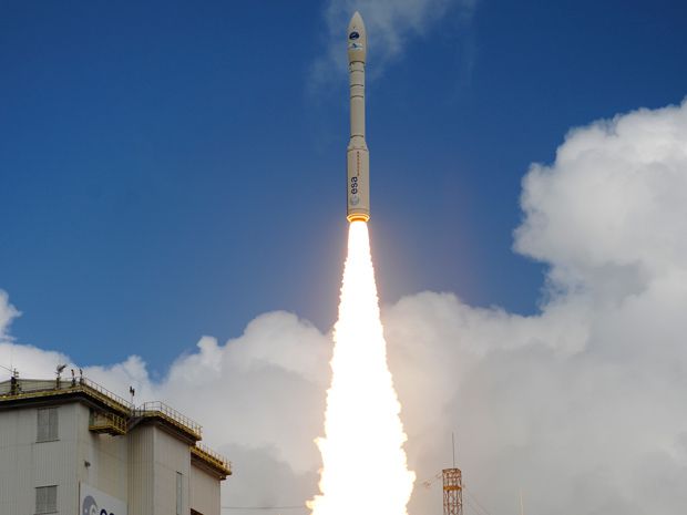 A cylindrical rocket blazes into a blue sky with some clouds shortly after takeoff