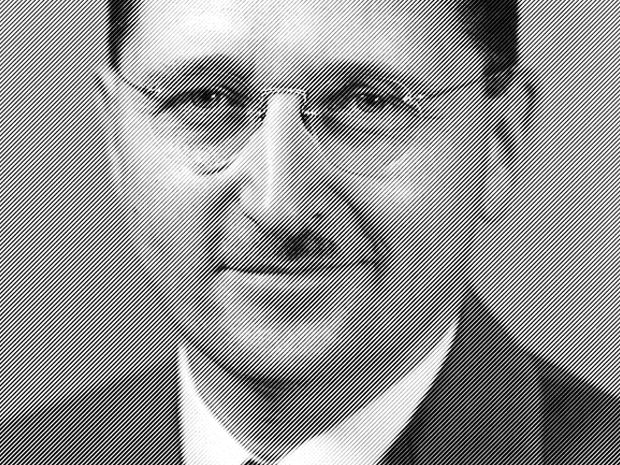 A black-and-white photograph of a middle-aged white man, with a round face and small mustache, wearing circular, rimless, eye glasses.