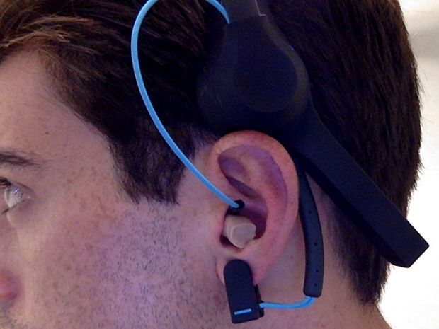 Man wearing an earplug-like device that's connected by a wire to a headset