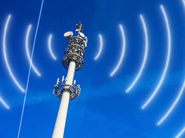 A silver tower lined with antennas against a clear blue sky broadcasts cellular signals.