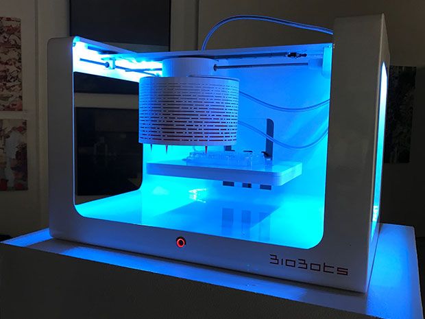 The bioprinter, a white box illuminated from within by blue light, lays down layers of materials to form a 3D tissue.