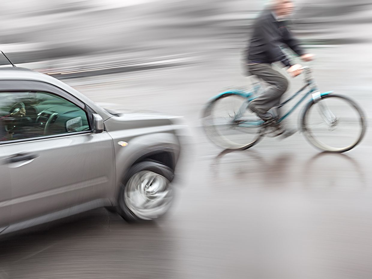 Photograph of a car and bicyclist nearly missing each other.
