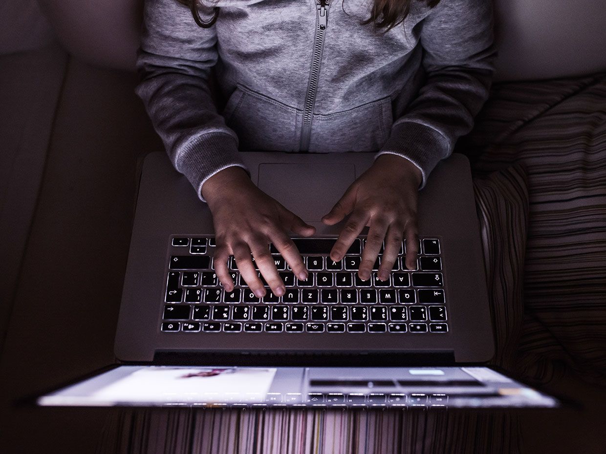Photograph showing the hands of a youth on a laptop.