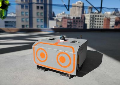 A small rectangular robot with large orange cartoon eyes on a construction site
