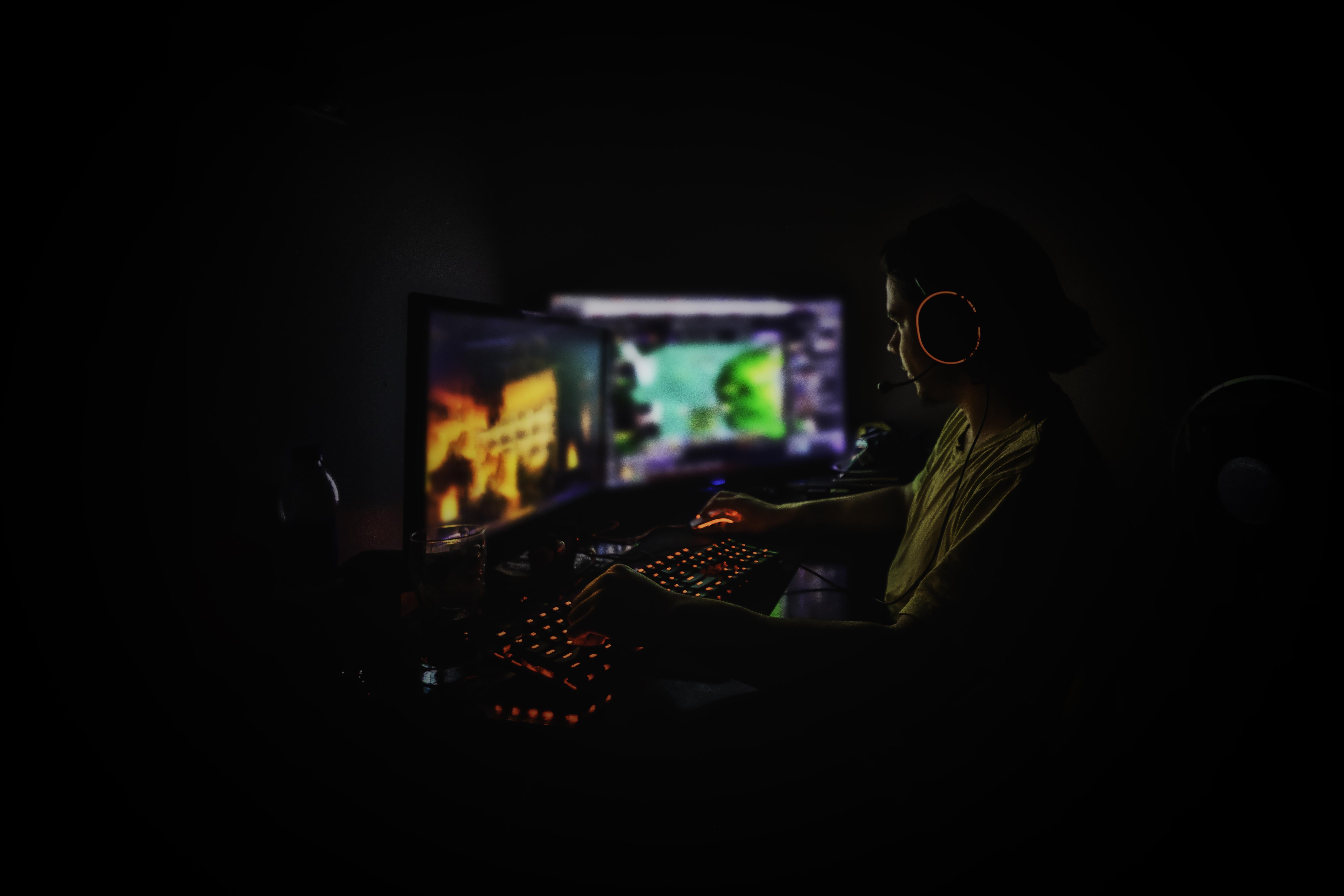 A man wearing a headset is seen in a dark room playing video games