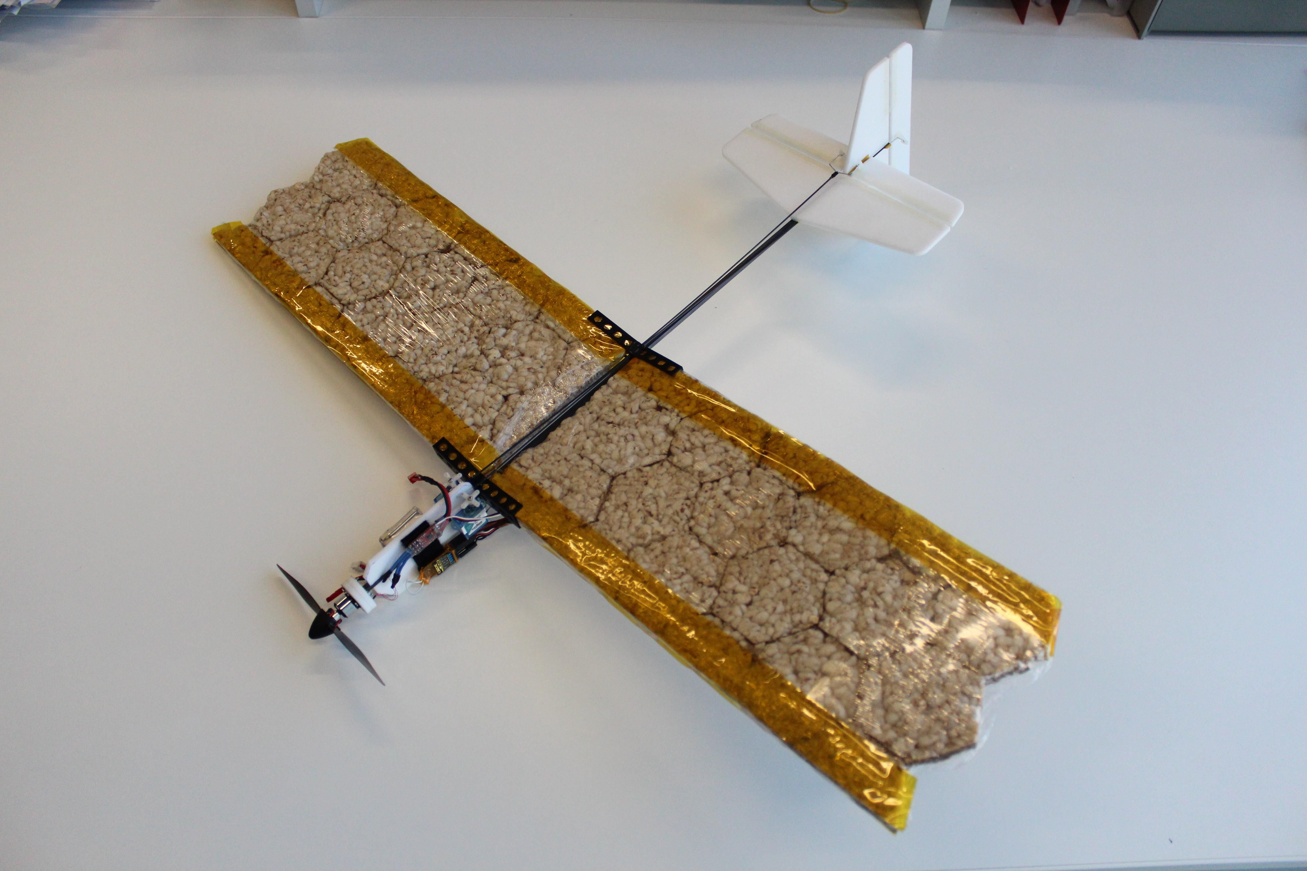 A drone airplane sits on a lab bench, it has a normal propeller and motor and tail but its wings are made of rice crackers covered in clear plastic