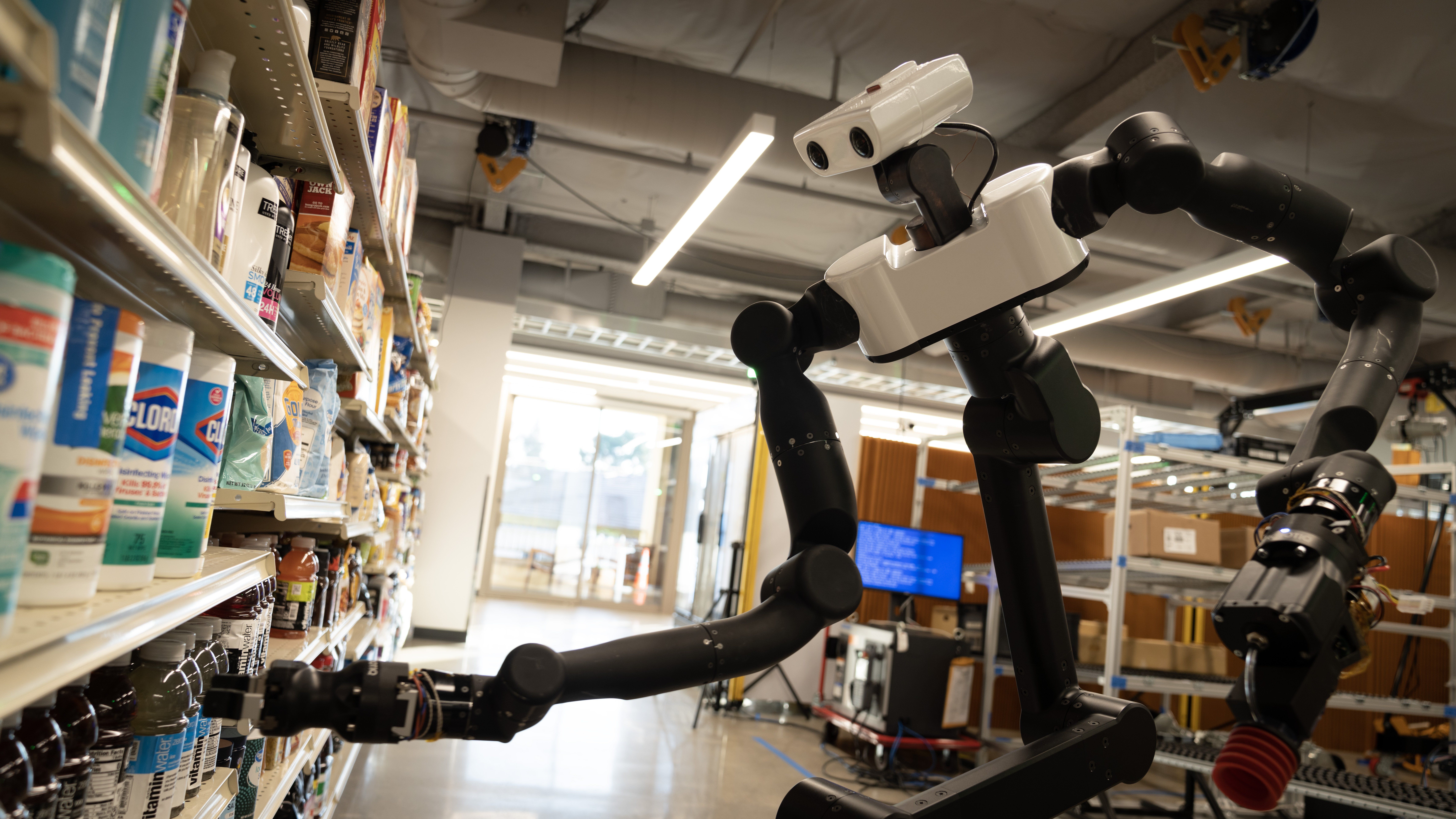 A black and white humanoid robot picks a bottle off of a shelf in a research lab