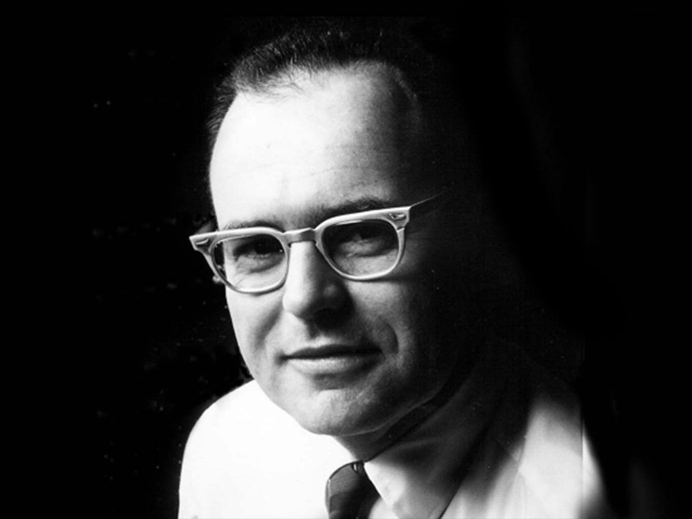 A black and white photo of a man in a tie and glasses.  