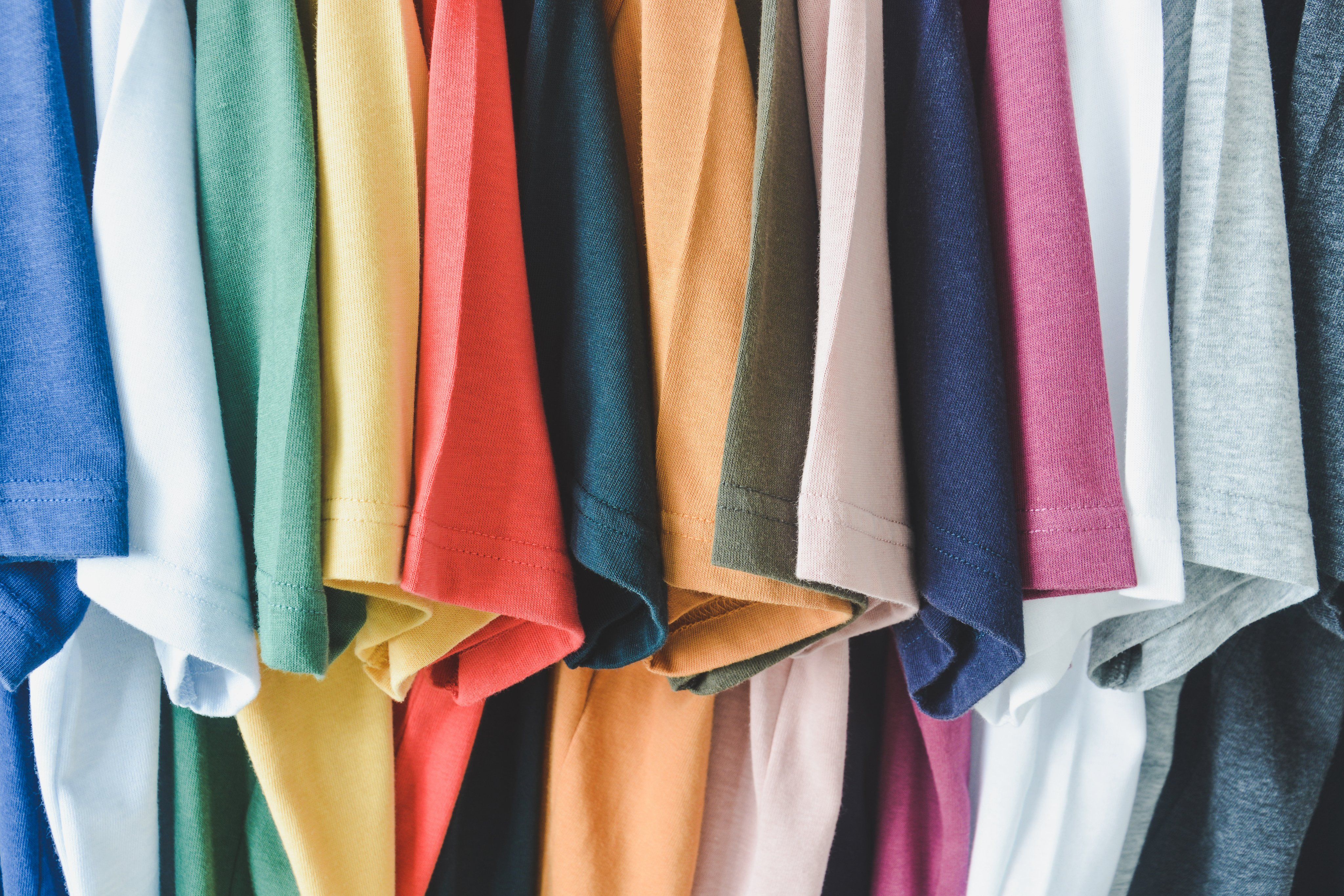 Short sleeve t-shirts of multiple colors including blue, green, yellow, red, orange, purple, pink, and gray, hang next to each other.