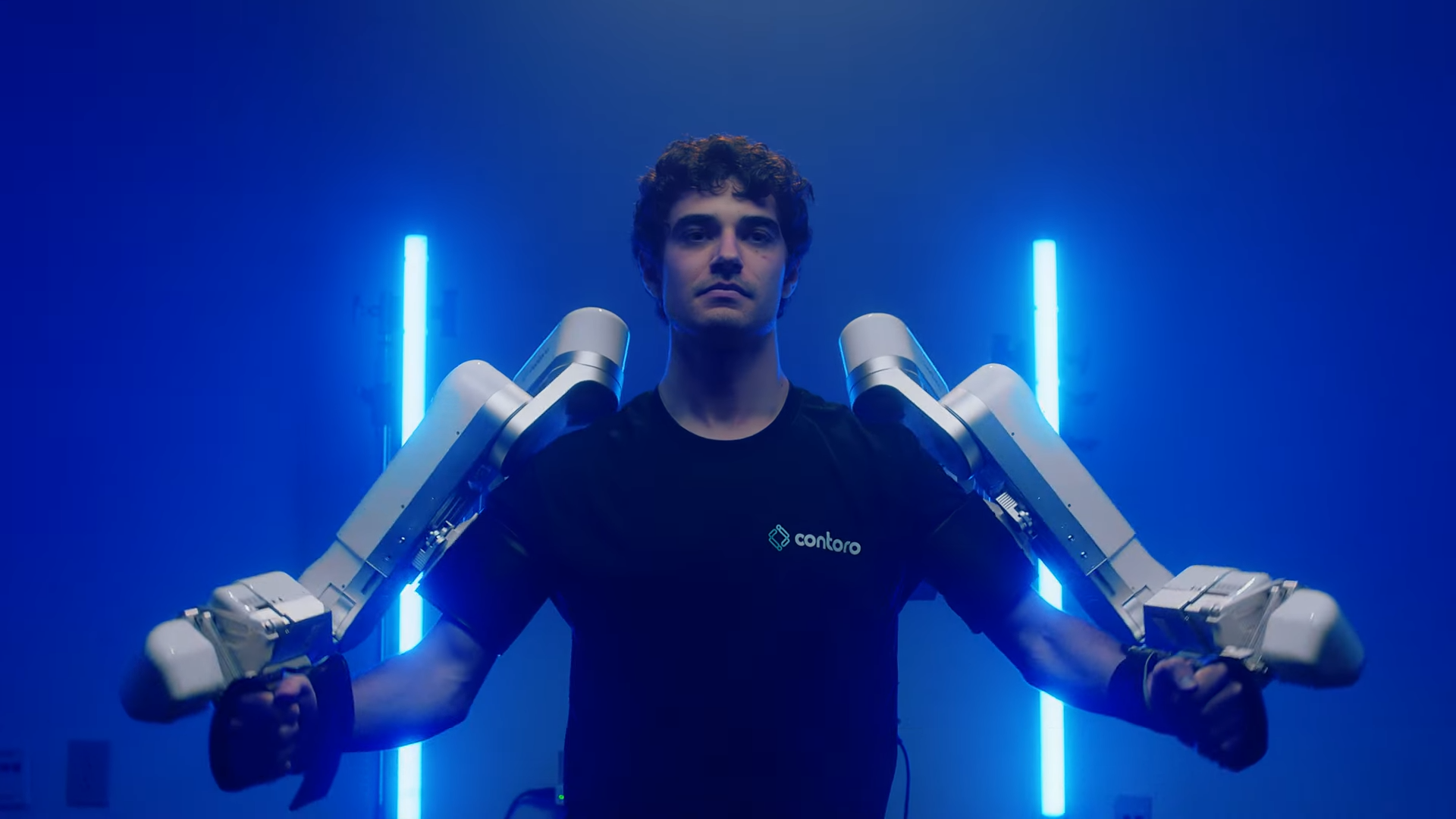 A photo of a human with two white robotic arms strapped to their arms 