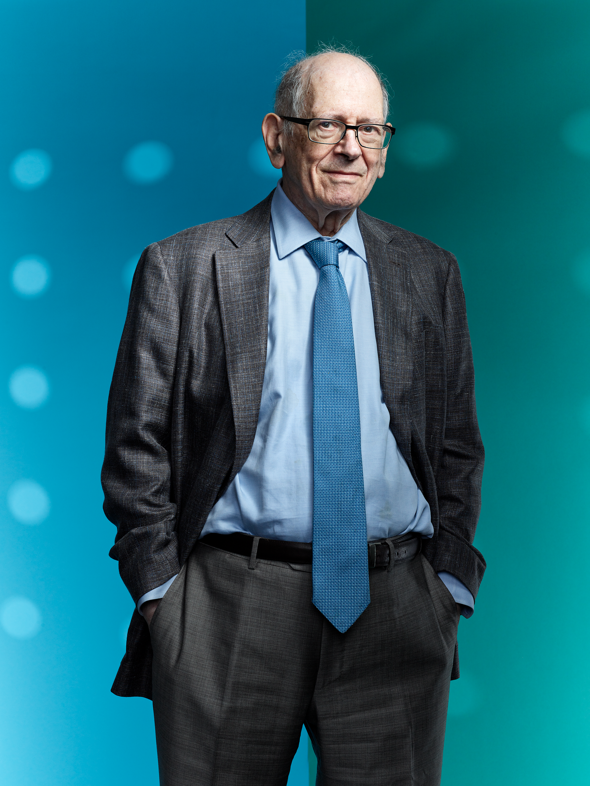 Photo of an older man in a dark suit in front of a blue and green background