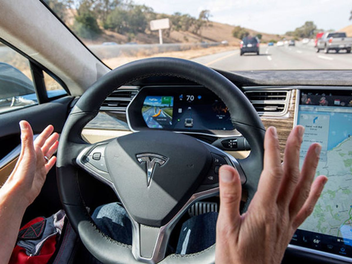 Interior view of the dashboard on a self-driving car driving on a road; the driver's hands are off the wheel