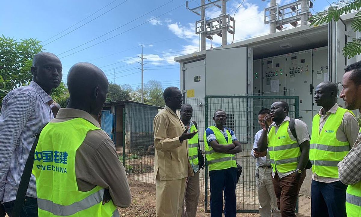 Jacob M. Deng, in a khaki suit, talks with utility workers during the commissioning of a substation in Juba, South Sudan.