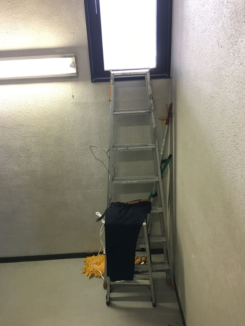 Ladder with mop propped next to it, a pair of men\u2019s trousers slung over a middle rung.