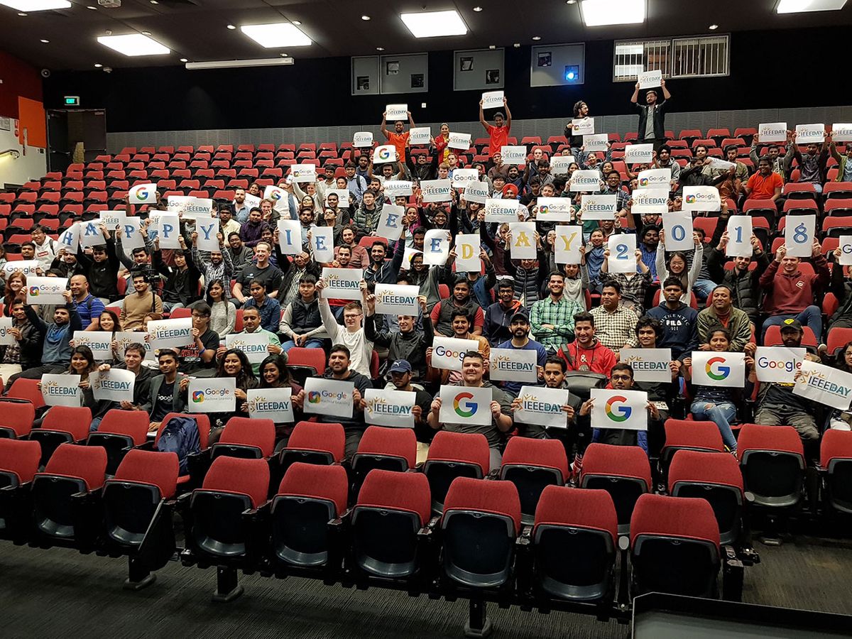 Large number of people from the IEEE La Trobe Student Branch in Melbourne, Australia holding signs including "Happy IEEE Day" and IEEE Day and Google logos.