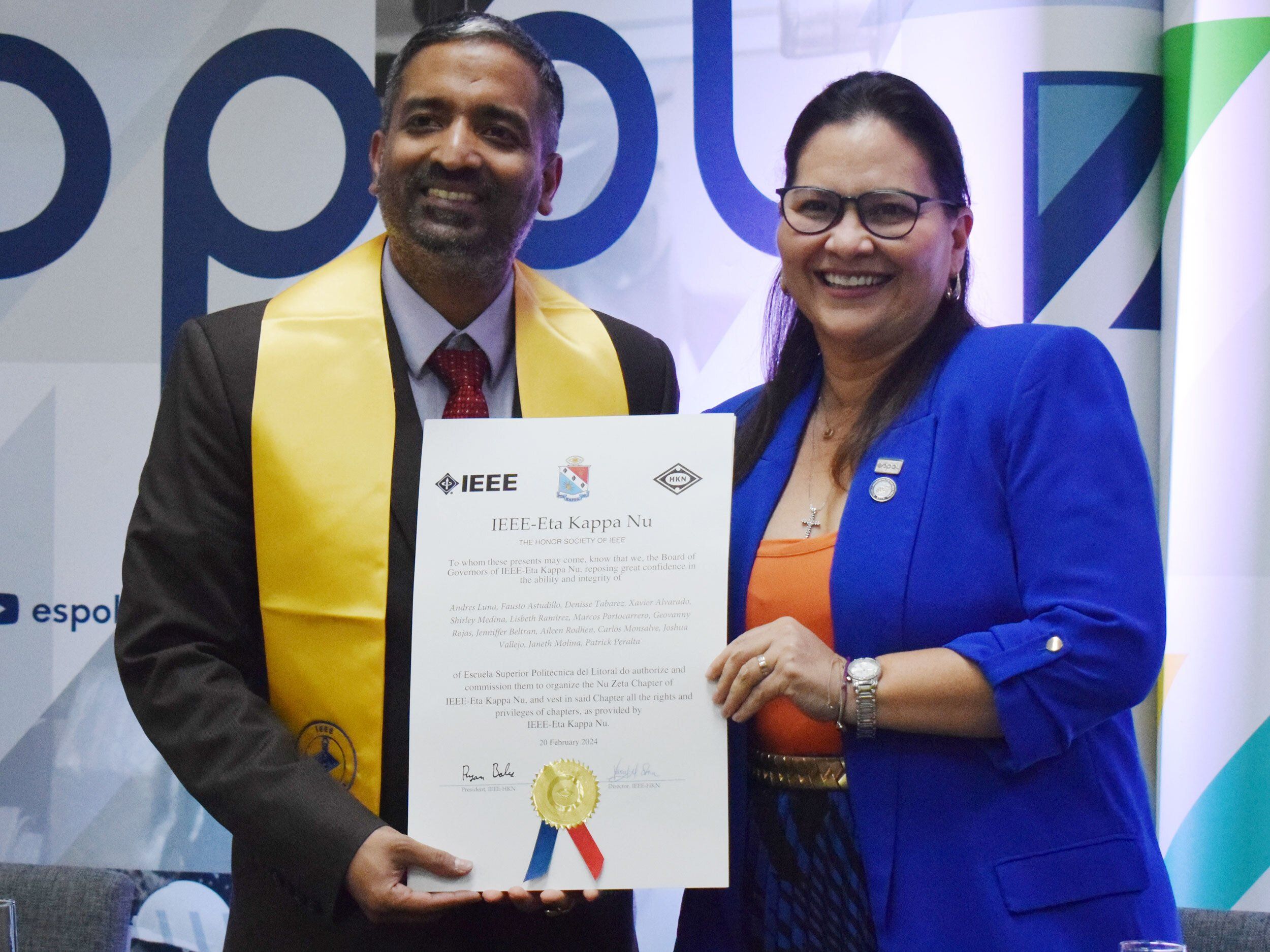 man and woman posing for a portrait smiling while holding a piece of paper with text and a blue and red ribbon with gold seal