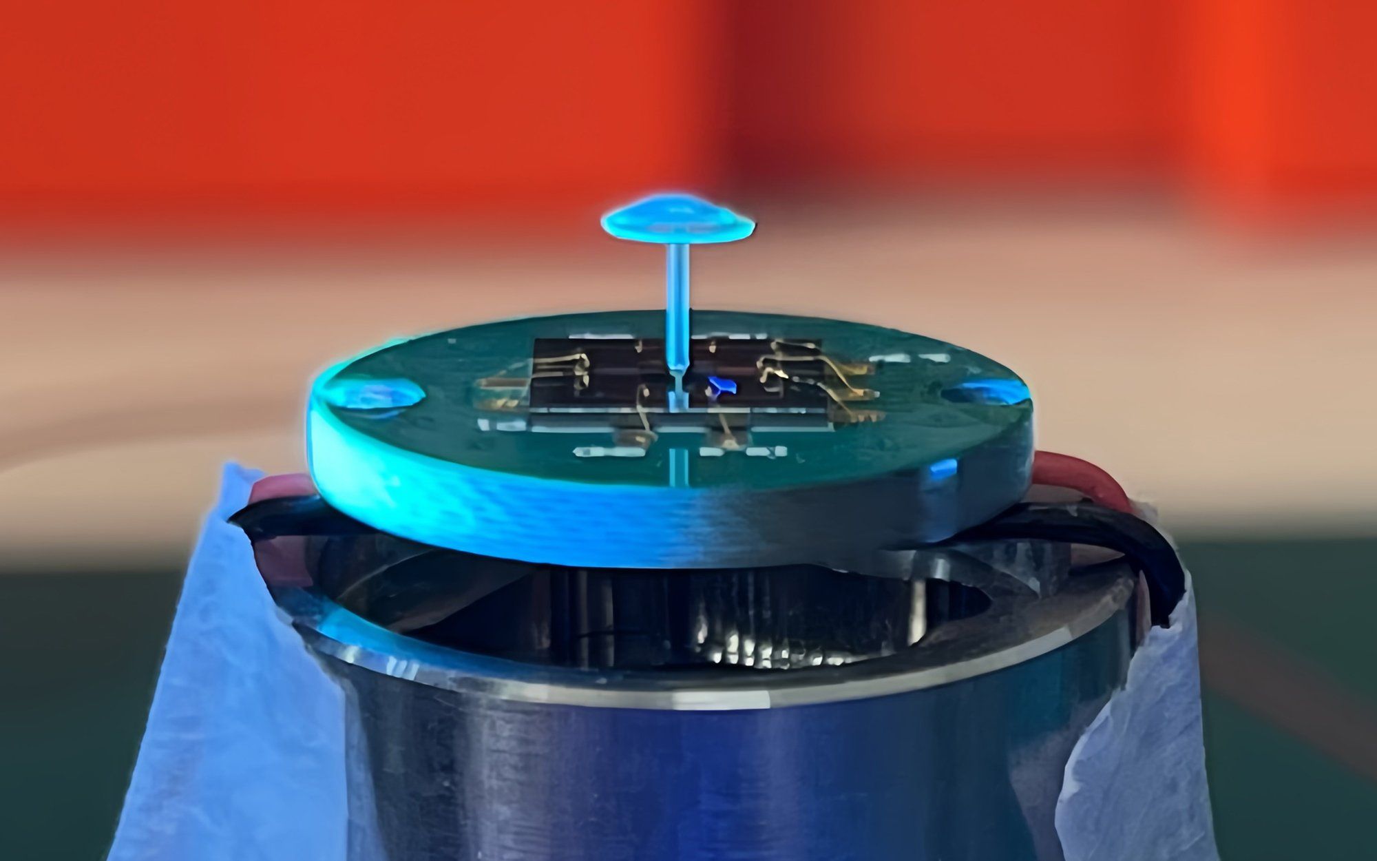 A device consisting of a circle with a chip on top and a mushroom shaped blue sensor standing upright on it. 