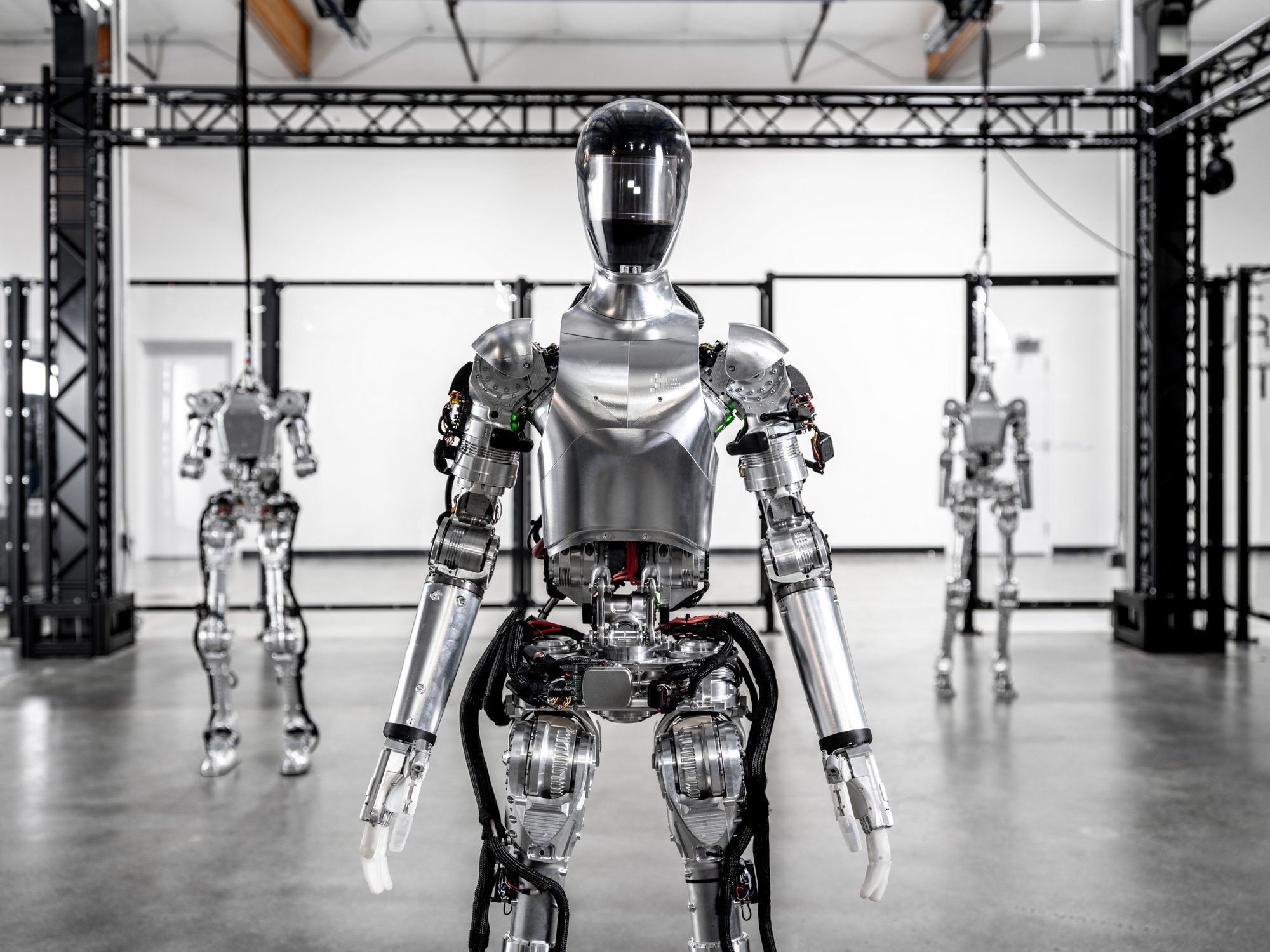 A photograph of a slim humanoid robot standing with reflective metal skin and a black motorcycle helmet.