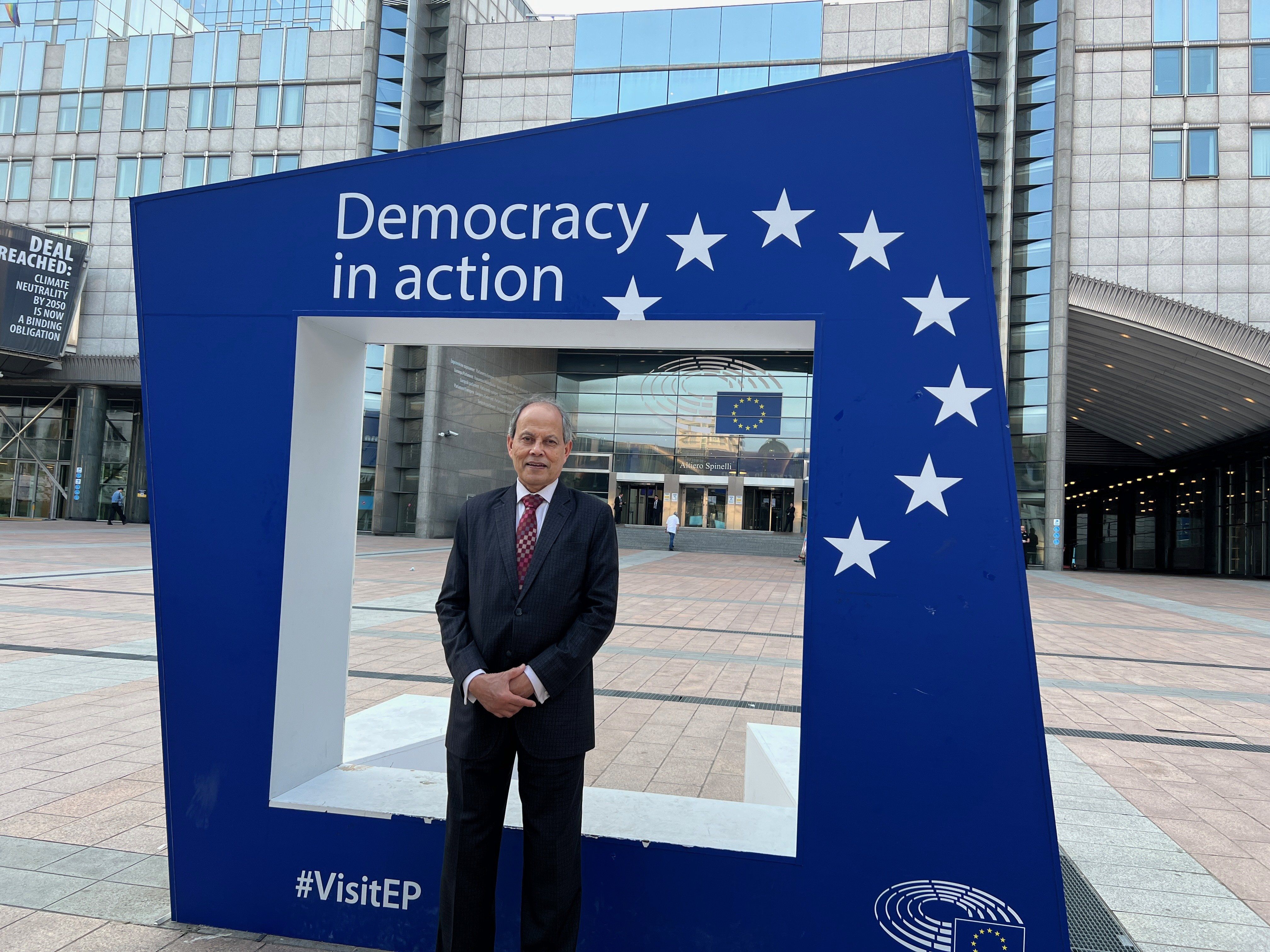 Photo of a man standing in front of a display that says "Democracy in action." 