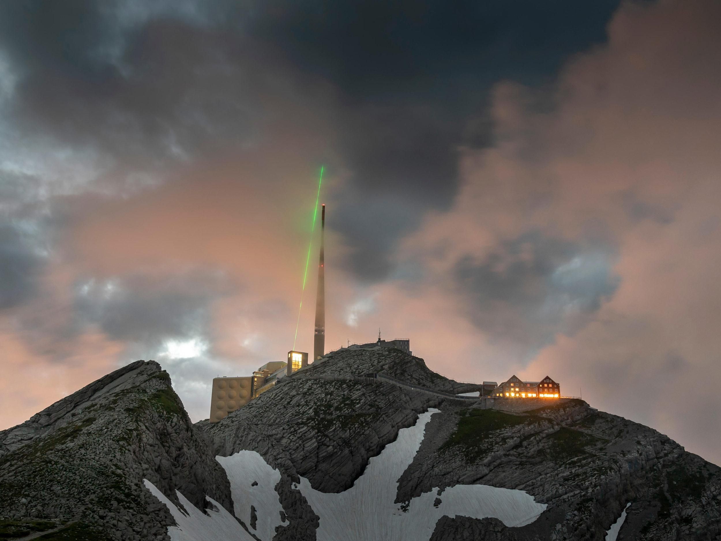 A green laser shooting up into a cloud-filled sky on the side of a cliff.