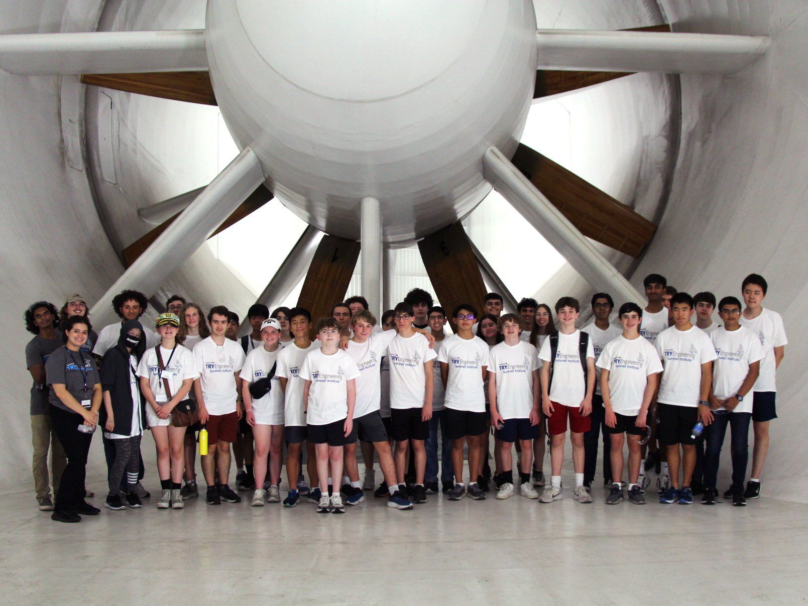 group of teenagers posing for a group photo in white t-shirts in front of a jet engine propeller